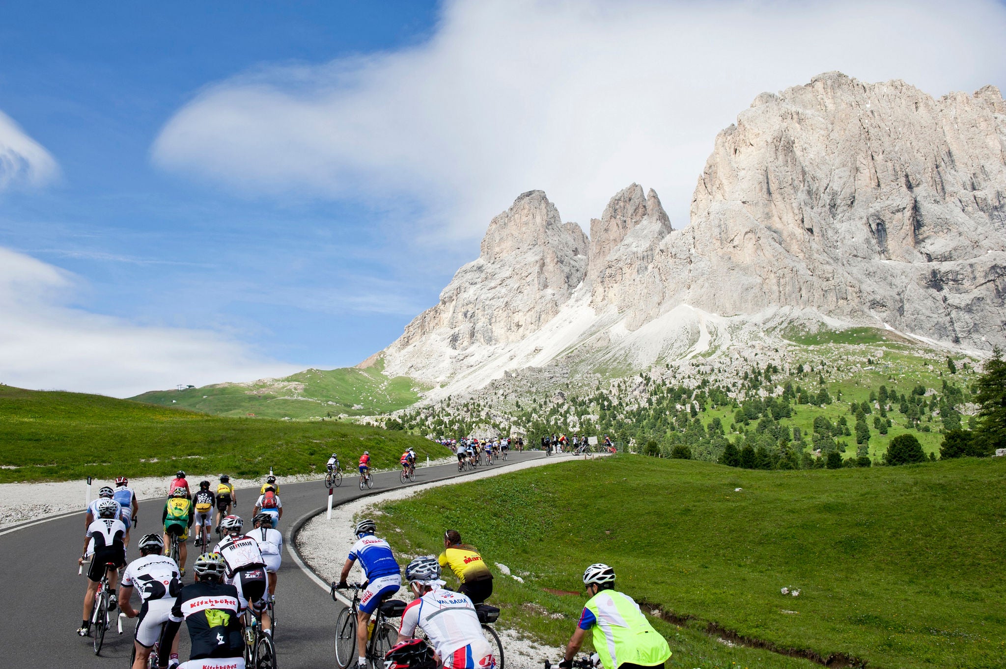 Etliche Rennradfahrer sind an einem Sommertag bei einem Wettkampf am Sellajoch vor dem Dolomitenpanorama unterwegs.