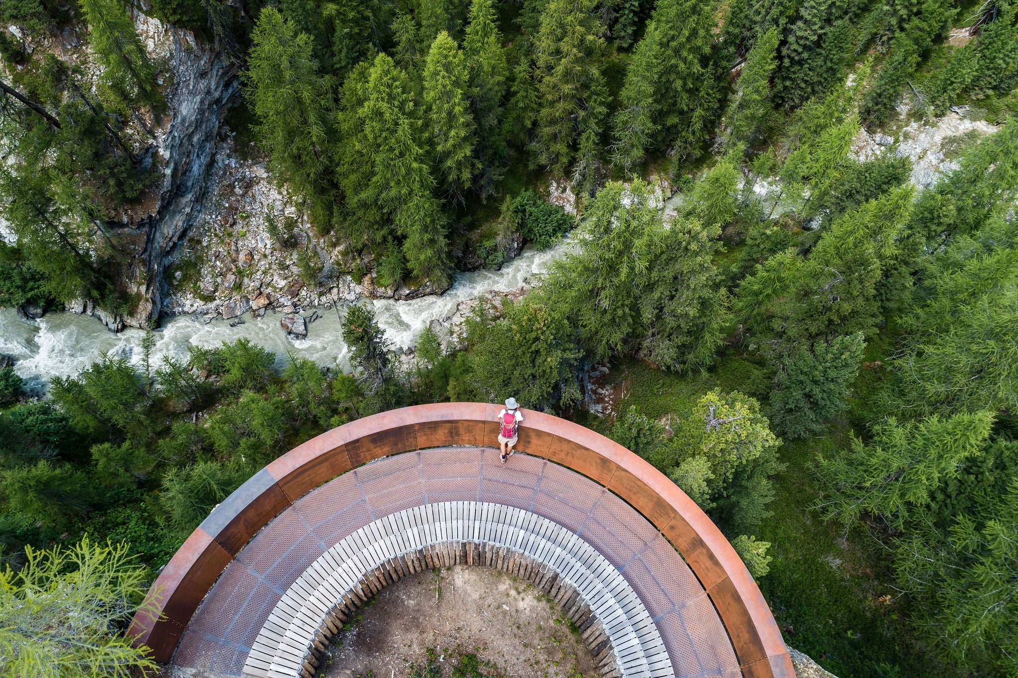 Eine Person steht auf einer Aussichtsplattform und blickt auf den Wald unterhalb bei Latsch Martell im Herbst