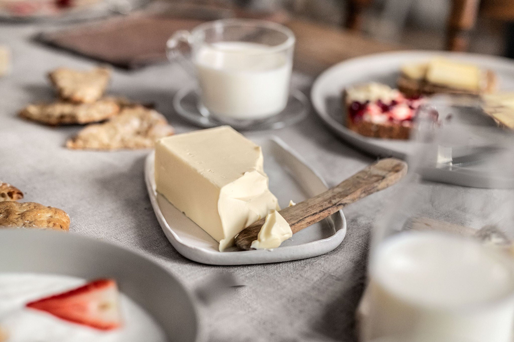 Ein rustikaler Tisch gedeckt mit Milchprodukten. Im Fokus steht rechteckiger Teller mit einem Stück Butter.