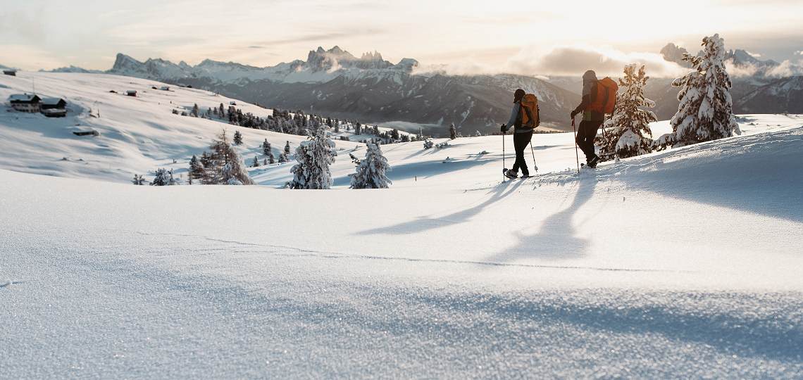 Zwei Personen wandern in Schneeschuhen über die verschneite Villanderer Alm, im Hintergrund die Dolomiten