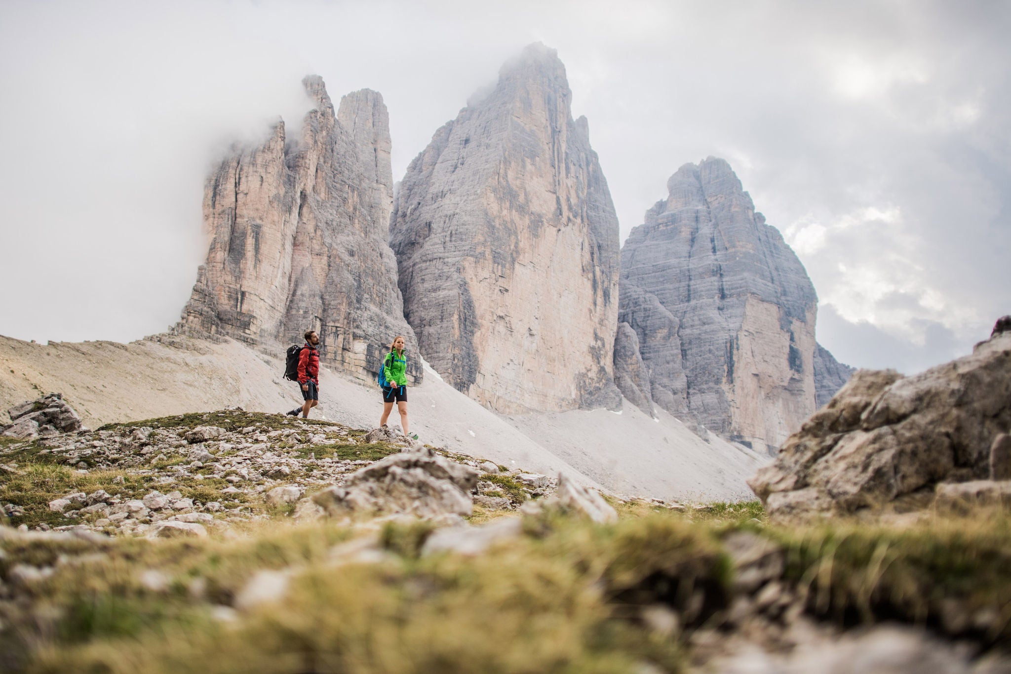 Ein Mann und eine Frau wandern in der Bergwelt der Dolomiten, die markanten Drei Zinnen im Hintergrund