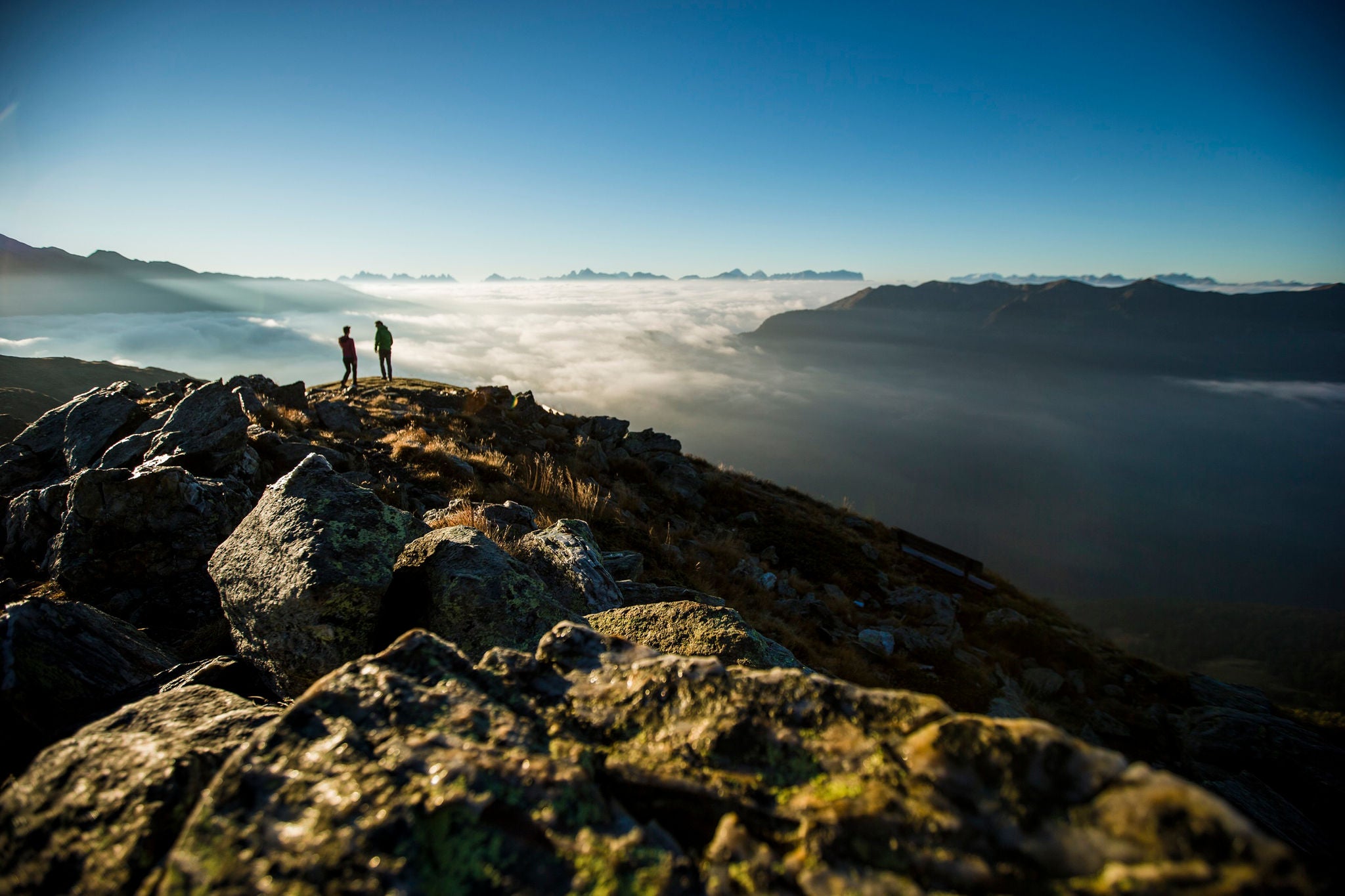 Zwei Personen auf dem Gipfel zu Sonnenaufgang mit Hochnebel und strahlend blauem Himmel