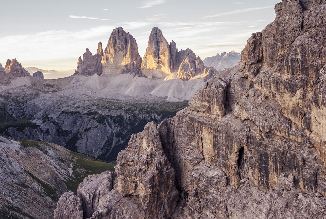 Blick auf das Bergpanorama der Dolomiten mit der majestätischen Formation der Drei Zinnen in der Bildmitte, von Sonne beschienen. 