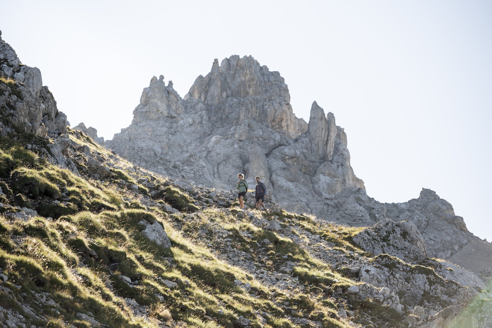 Ein Mann und eine Frau wandern über einen Bergpfad hinunter, hinter ihrem Rücken erhebt sich ein markanter Dolomitenfelsen