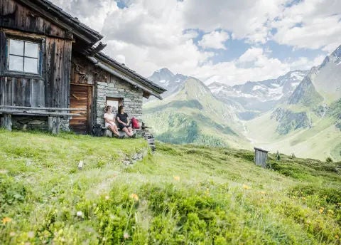 Zwei Personen sitzen auf einer Bank vor einer Hütte