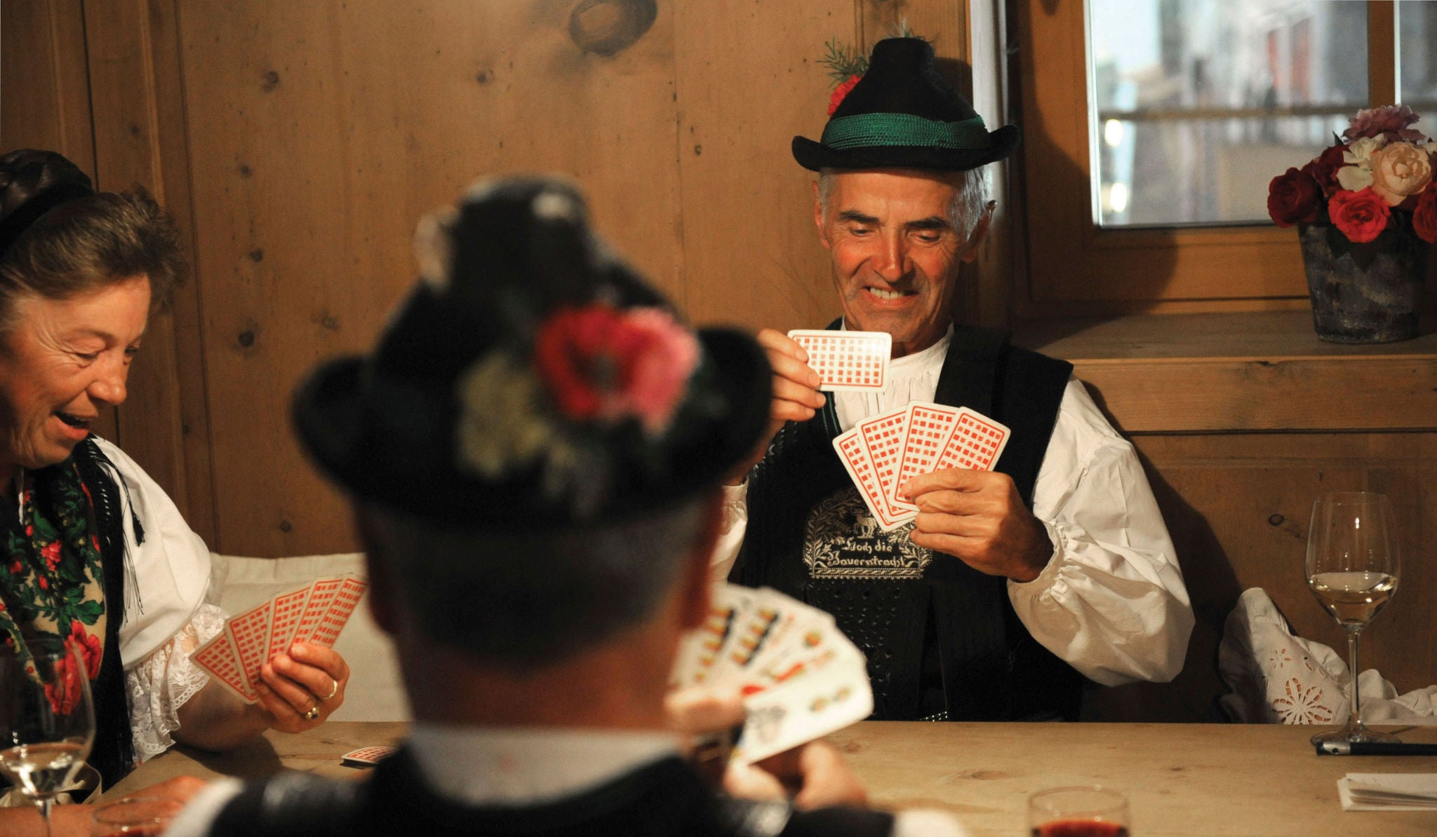 Drei Personen in traditioneller Tracht am Stubentisch beim "Watten" - ein typisches Kartenspiel in Südtirol