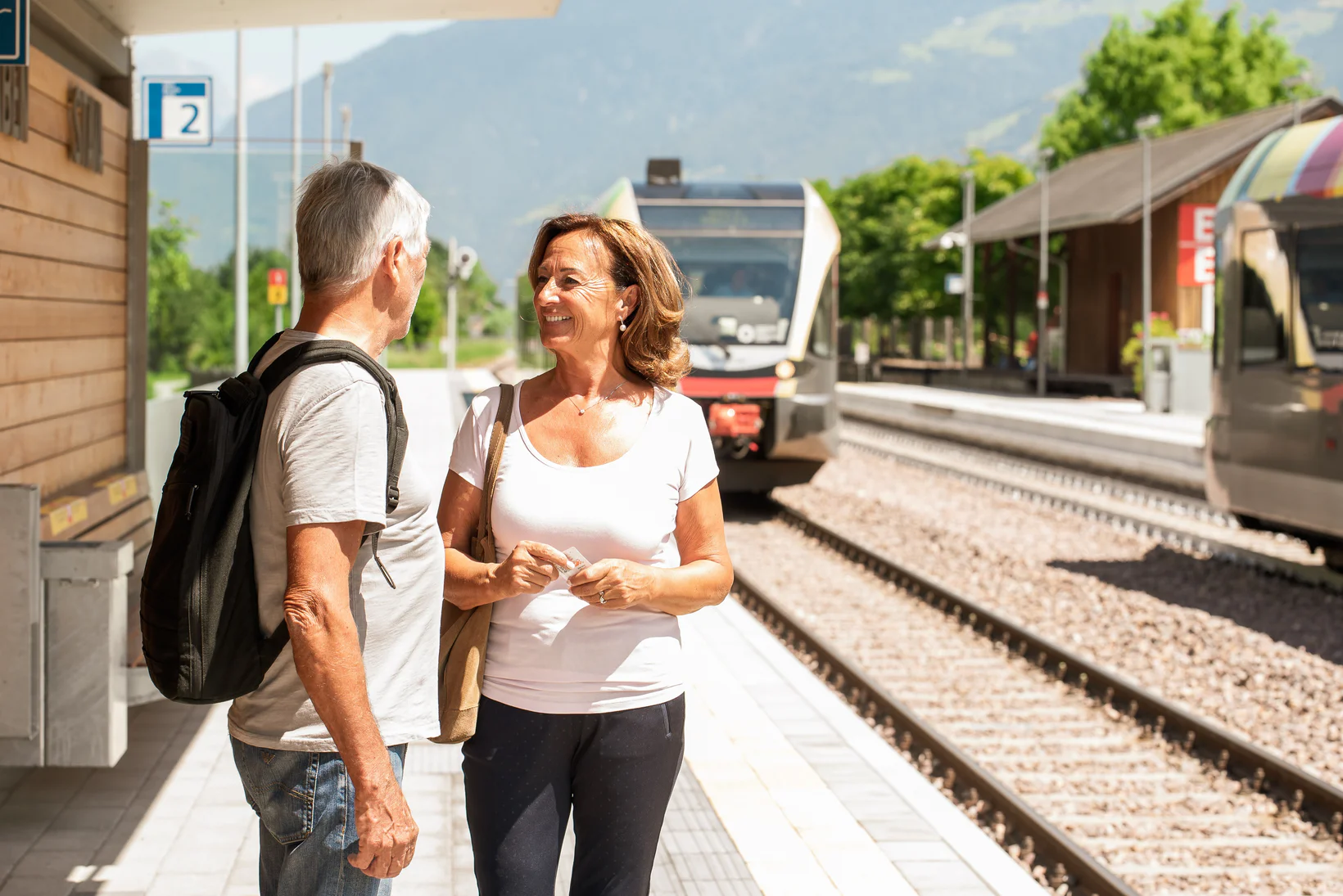 Un uomo e una donna attendono l'arrivo del treno in una stazione immersa nel verde