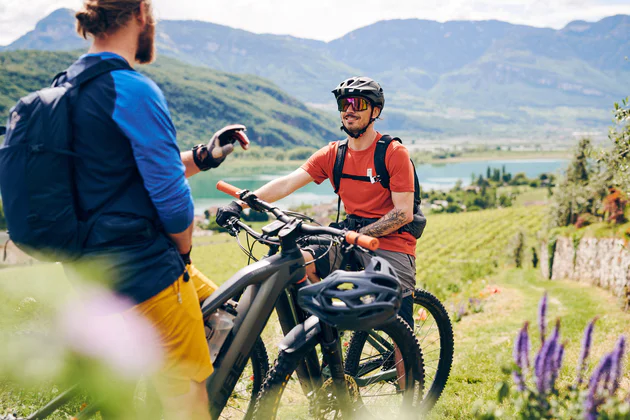 Due ragazzi in mtb fanno una pausa su un percorso ciclistico vinicolo che affianca vigneti e il lago di Caldaro