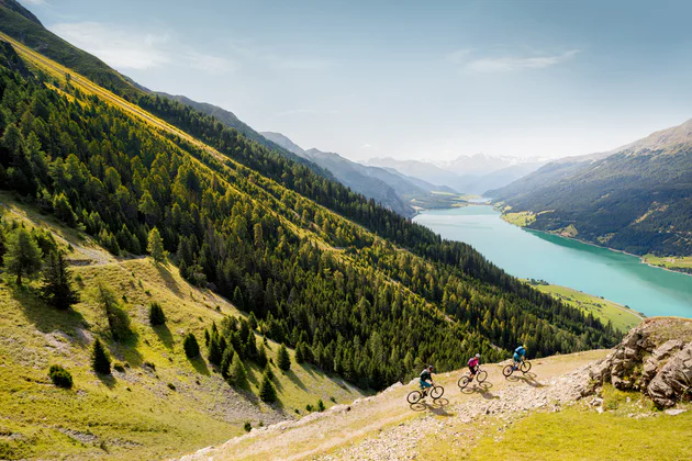 Žena a muž jedou na svých horských kolech nad jezerem Reschensee.