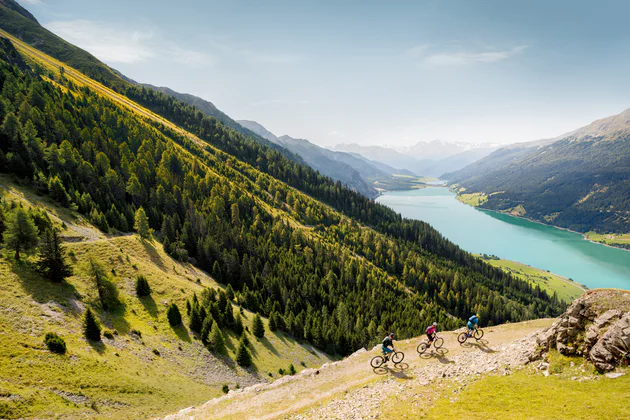 Eine Frau und ein Mann fahren auf ihrem Mountainbike oberhalb des Reschensees.