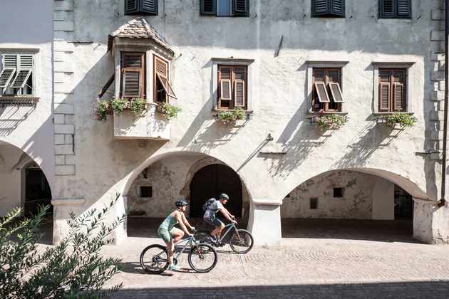 Due persone passano in bicicletta davanti ai portici di Egna