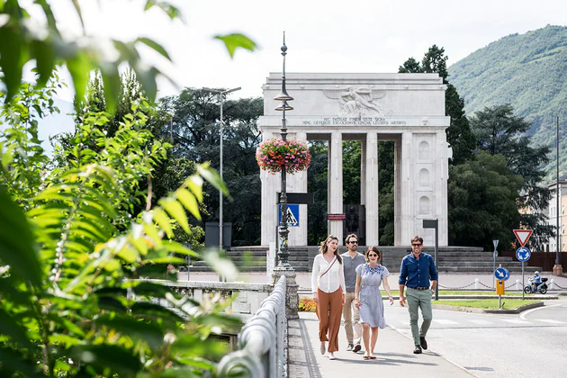 Een groep loopt over de Talvera-brug met het Overwinningsmonument op de achtergrond voor een stadswandeling in Bolzano.