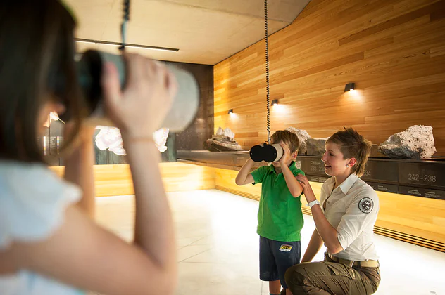 Assieme all'assitente due bambini si divertono con il cannocchiale nel centro visite del Parco naturale Puez-Odle