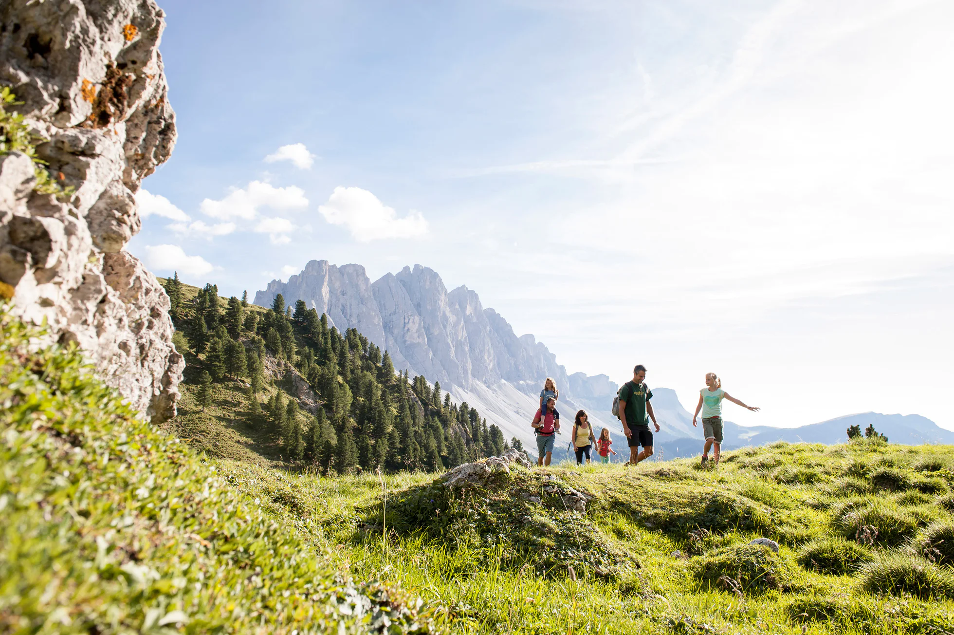 Una famiglia in escursione in Val di Funes, alle loro spalle dolomitiche cime delle Odle