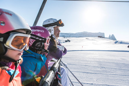 Primo piano di due bambine e di una donna con casco e occhiali da sci con panorama innevato