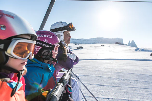 Primo piano di due bambine e di una donna con casco e occhiali da sci con panorama innevato