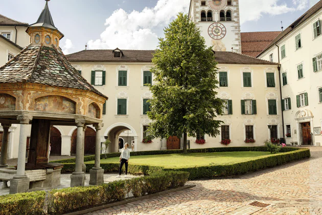 Vista sul cortile interno dell'Abbazia Agostiniana di Novacella, in primo piano il chiostro con il pozzo e una visitatrice interessata