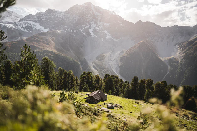 Vista di un'idilliaca baita di montagna immersa nel verde e contornata da imposanti montagne