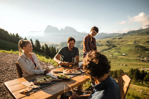 Cztery osoby siedzą wspólnie przy jedzeniu, w tle widać dolinę