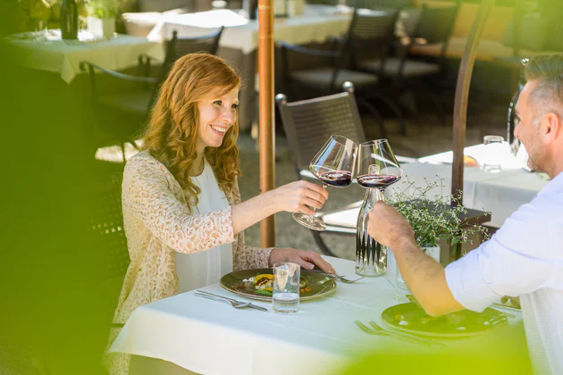 Deux personnes à la table d'un restaurant, en train de trinquer avec un verre de vin rouge.