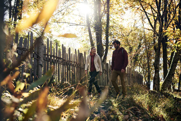 A man and a woman walk along a fence under autumnal trees through the Eisack Valley.