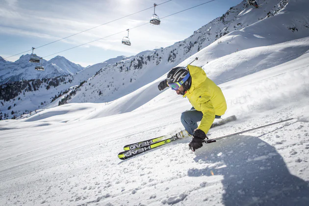 Skifahrer in neon-gelber Jacke fährt Piste hinunter