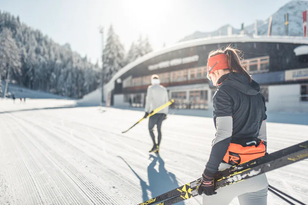 Deux personnes en train de marcher dans la neige, avec des skis de fond à la main