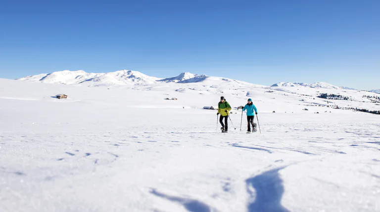 Two people walking through a winter landscape in the mountains.