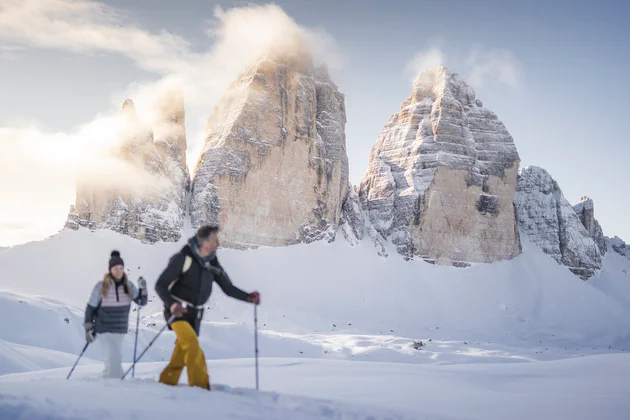 A man and a woman making a winter hike in the snow, in the background the Three Peaks