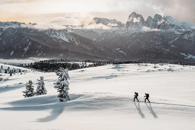 A man and a woman making a winter hike in the snow, in the background the Three Peaks