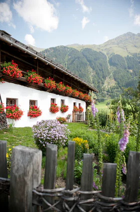 Ein Bauernhaus mit roten Blumen an den Fenstern, im Hintergrund grüne Hügel