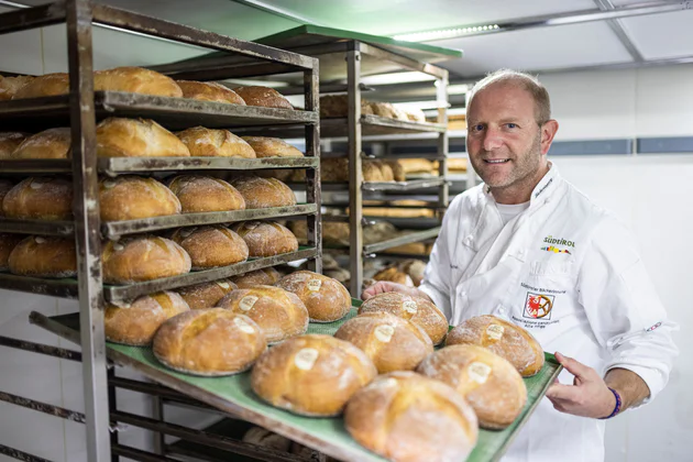 Piekarz Hannes Schwienbacher wyciąga z regału blachę pełną bochenków Ultner Brot.