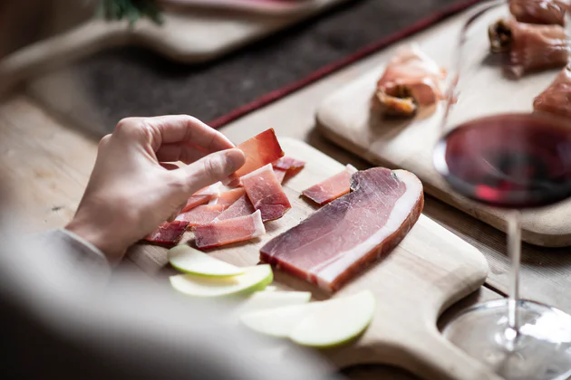 Ein Brett Speck mit Südtiroler Speck, daneben ein Glas mit Rotwein