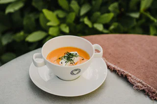 Eine Tasse mit cremiger Karottensuppe, garniert mit einem Klecks Sahne und frischen Kräutern.
