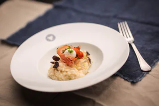 Cremiges Risotto auf einem Teller, garniert mit Schinkenscheiben, einem Frischkäsehäubchen und frischen Kräutern.