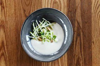 Eine cremige Suppe in einem dunklen Teller, garniert mit dünnen Apfelstreifen, Sellerie, Walnüssen und frischen Kräutern.