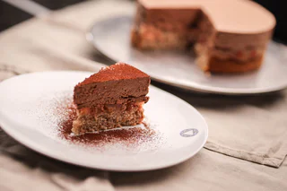 Ein Stück Schokoladenmousse-Torte auf einem weißen Teller, mit Kakaopulver bestäubt.