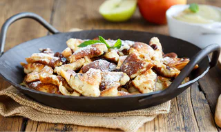 Ein Pfännchen voller Kaiserschmarrn mit Rosinen, bestäubt mit Puderzucker und garniert mit einem Minzblatt.