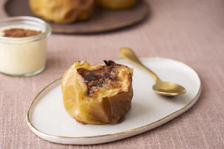 Ein gebackener Apfel mit Zimt und Zucker auf einem weißen Teller mit goldfarbenem Löffel.