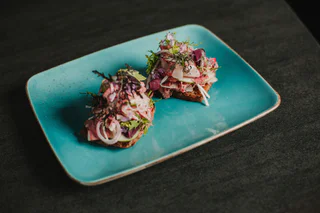 Zwei kunstvoll belegte Brotscheiben mit Wurst, Zwiebeln und buntem Salat.
