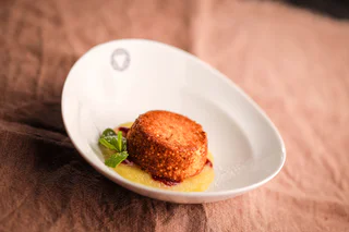 Ein goldbraunes Dessertbällchen auf Apfelmus mit roter Fruchtsauce und Minzblatt, serviert in einem weißen Teller.