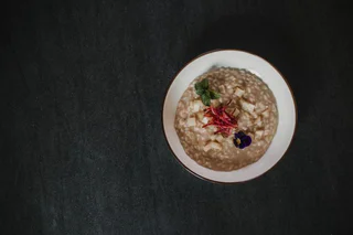 Cremiger brauner Risotto mit gewürfeltem Käse, frischen Kräutern, roten Streifen und einer essbaren Blüte.