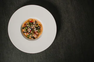 Ein tiefes weißes Teller mit einem kunstvoll angerichteten Gericht aus Gemüsewürfeln, Kräutern und heller Soße.