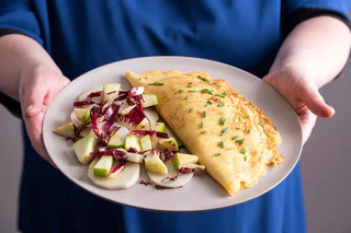 Teller mit Omelett bestreut mit Schnittlauch, serviert mit Apfel-Radicchio-Salat und weißen Gemüsescheiben.