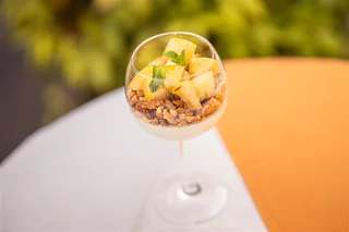 Dessertglas mit heller Creme, knusprigen Streuseln, frischen Ananasstücken und Minze.