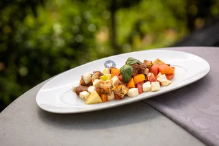 Bunter Brotsalat mit Obststücken, Käsewürfeln und Basilikumblättern auf einem weißen Teller.