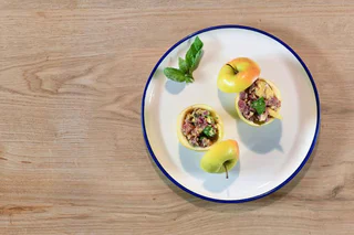 Gefüllte Äpfel mit Nussmischung und Minze, serviert mit Basilikum auf einem weißen Teller mit blauem Rand.