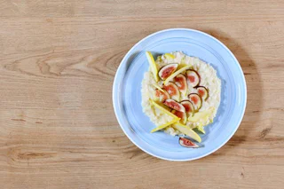 Cremiges helles Risotto mit Feigenscheiben und dünnen Apfelspalten auf blau-weißem Teller.