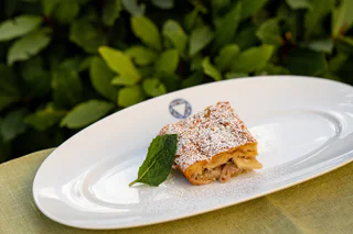 Ein Stück Scheiterhaufen mit Puderzucker bestreut, serviert auf einem weißen Teller mit einem Minzblatt, im Freien.
