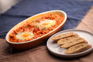 Ofengericht mit pochierten Eiern in einer würzigen Tomatensauce, garniert mit Kräutern und serviert mit knusprigem Brot.